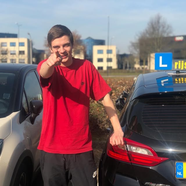 Leerling in een rood shirt naast een zwarte Meteor-lesauto.