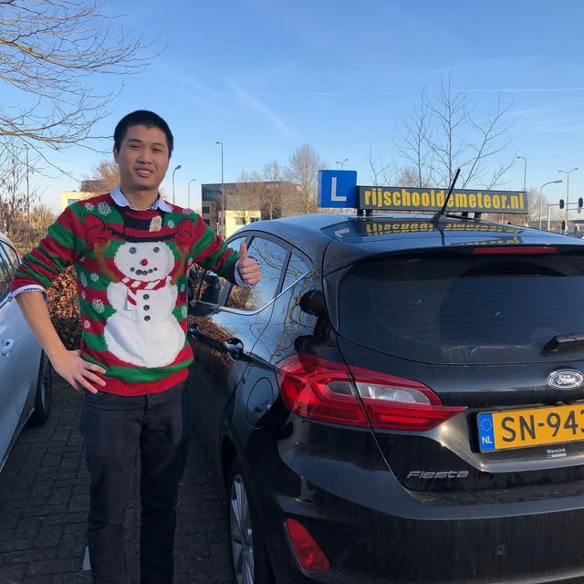 Leerling in een kersttrui naast de Meteor-lesauto.