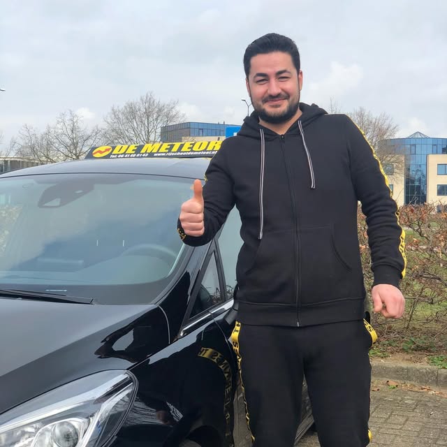 Leerling in een donkere trui met opgestoken duim bij de Meteor-lesauto.